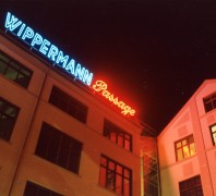 Gebäudeteil des Historischen Centrums bei Nacht. Auf dem Dach befindet sich Leuchtreklame. Links in blauer Schrift: "Wippermann" rechts daneben in rot "Passage".
